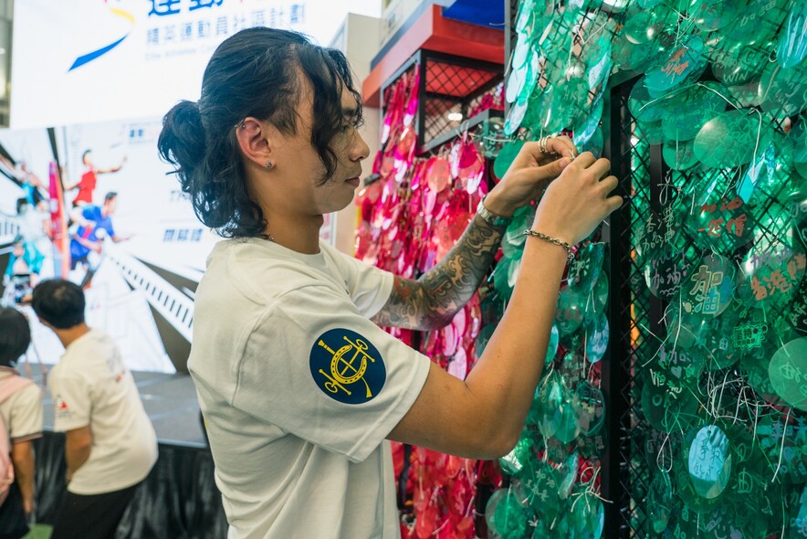<p>Lau Chi-lung, Ho Wai-hang, Lee Ka-to and Lee Sze-wing write their own messages of support for Team Hong Kong athletes to hang on the large cheering net. The net was a feature at all four stops of the roving exhibition for members of the public to offer their support to the athletes.</p>
