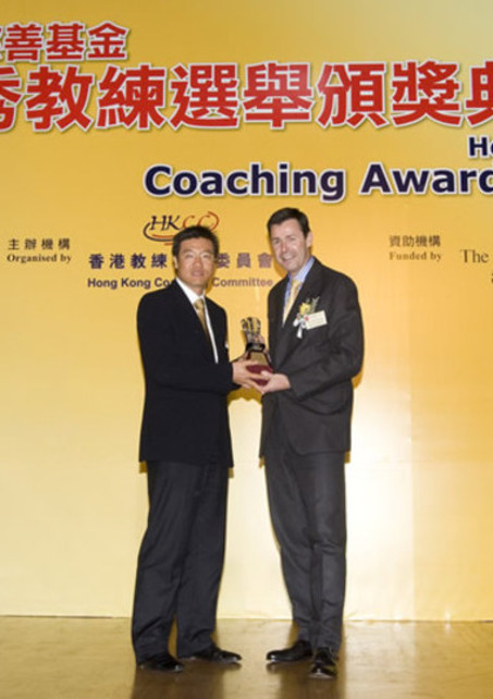帶領香港足球隊勇奪2009東亞運動會（東亞運）金牌的教練金判坤（左），從香港上海滙豐銀行有限公司香港區總裁馬凱博（右）手上接過最佳隊際運動教練獎。其他東亞運的教練亦獲邀出席頒獎禮，接受在場嘉賓的掌聲嘉許。
